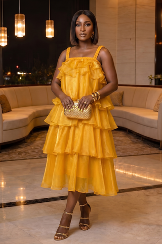Woman in a yellow dress standing in an indoor setting with beige sofas and decorative lights.