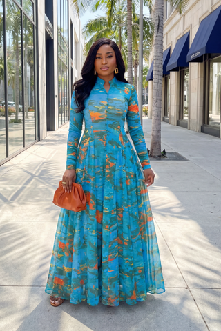 Woman in a blue floral dress standing on a city street with palm trees in the background