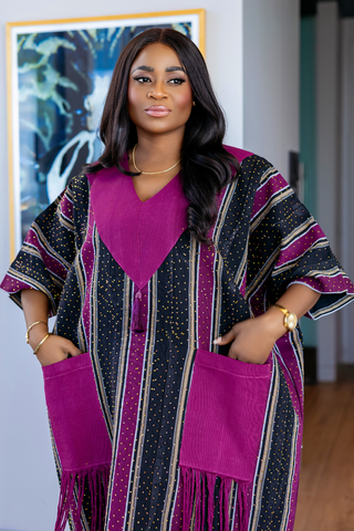 A woman wearing a magenta and black patterned kaftan dress with fringe and pockets, standing in an indoor setting.