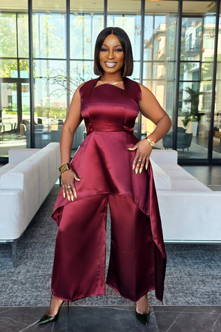 Woman in a burgundy jumpsuit standing in a modern indoor setting with large windows.