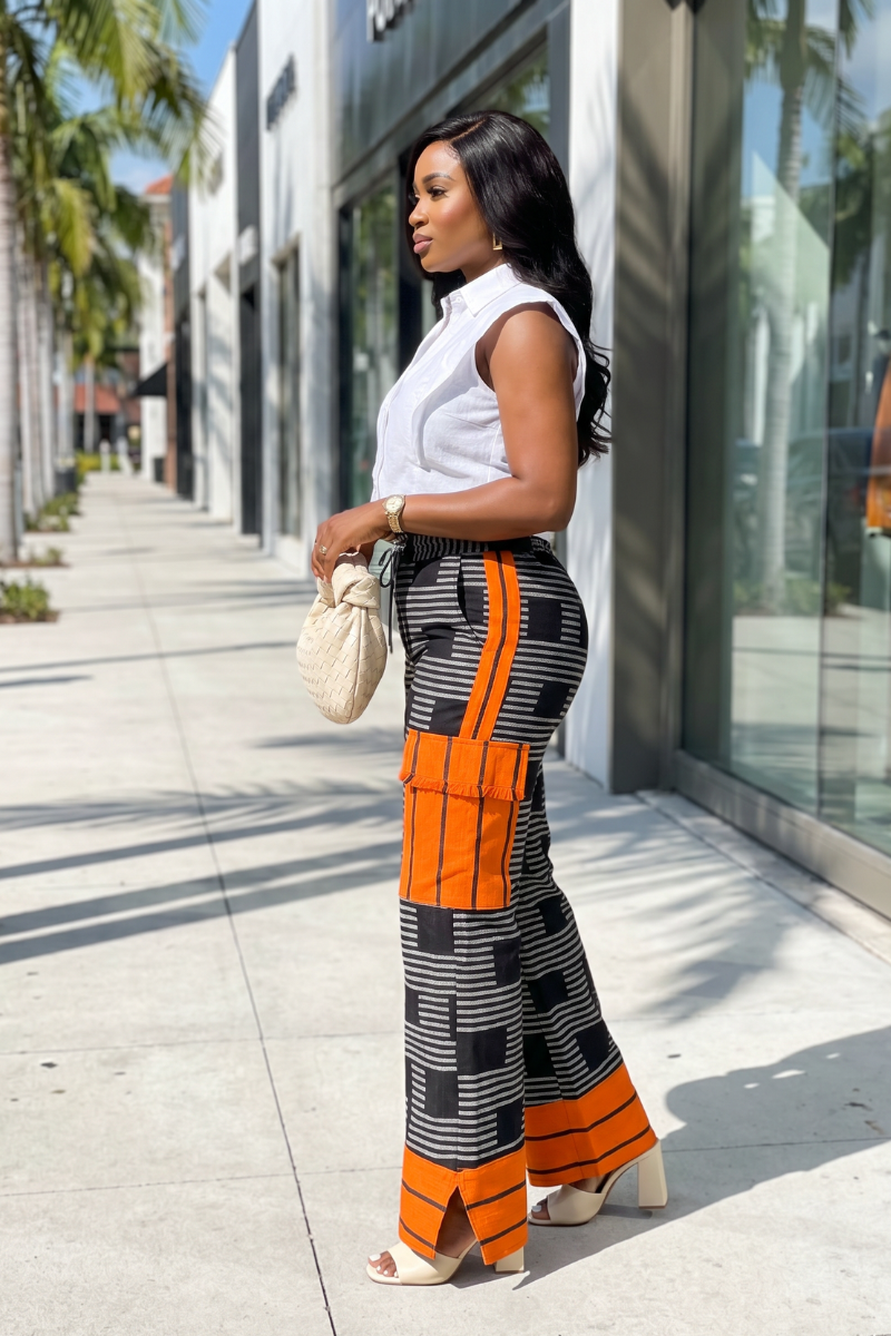 Woman in white top and orange and black patterned pants walking on a sidewalk.