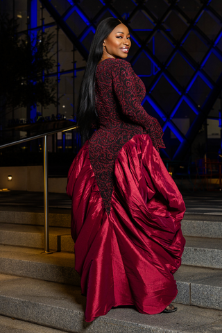 Woman in a red evening gown with black lace details standing on steps.