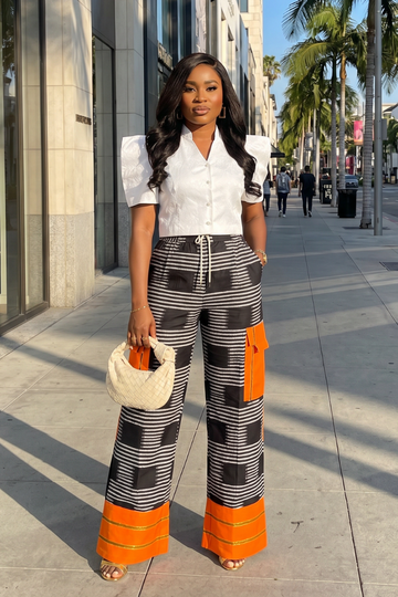 Woman in a stylish outfit with white shirt and patterned pants standing on a city street.