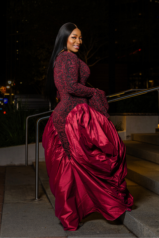 Woman in a red evening gown sitting on steps at night.