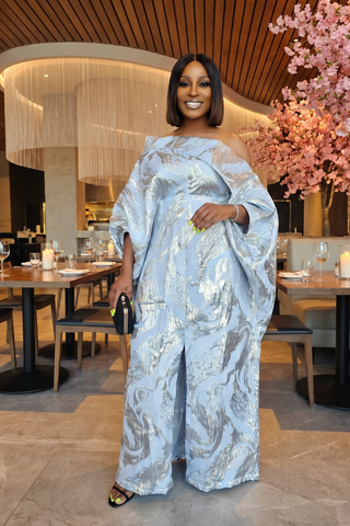 Woman in a light blue patterned outfit standing in a restaurant with pink floral decorations.