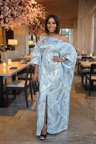 Woman in a light blue off-shoulder dress standing in a modern restaurant setting.