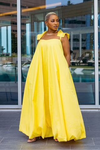 Woman wearing a yellow dress standing in front of a modern building with glass windows.