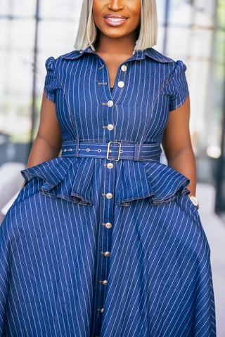 A woman wearing a blue pinstriped shirt dress with short puff sleeves, a button front, and a matching belt with a gold buckle.