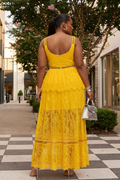 Woman in a yellow lace dress walking on a sidewalk with trees and buildings in the background.
