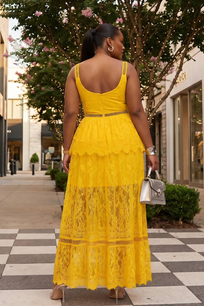Woman in a yellow lace dress walking on a sidewalk with trees and buildings in the background.
